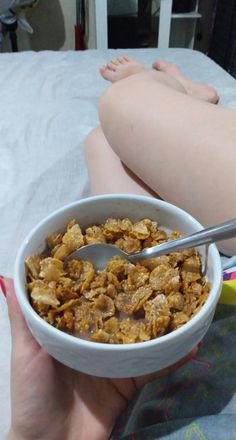 a person holding a bowl of cereal on top of a bed