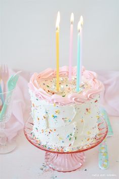 a birthday cake with white frosting and pink icing has five lit candles on it