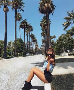 a woman is sitting on a bench in front of palm trees and talking on her cell phone