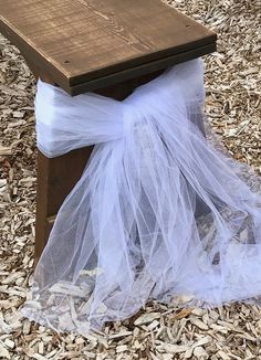 a wooden bench covered in white tulle sitting on top of wood chips