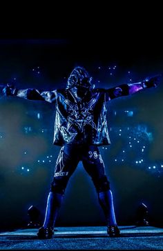 a man standing on top of a stage with his arms outstretched in the air and lights behind him