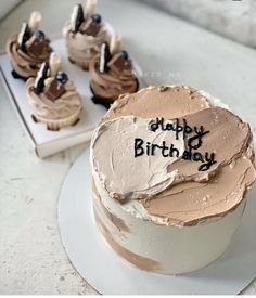 a birthday cake with chocolate frosting sitting on top of a table next to other cupcakes