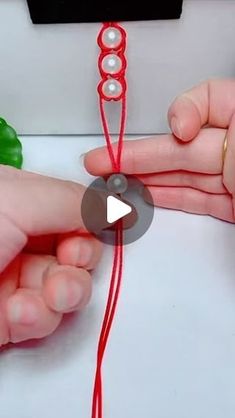 two hands are working on something with red string and beads, while another hand is holding the string