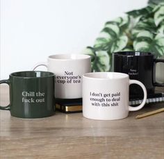 three coffee mugs sitting next to each other on top of a wooden table with plants in the background