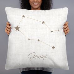 a woman holding up a pillow with the zodiac sign gemini on it and smiling at the camera