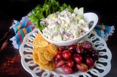 a plate with grapes, crackers and salad on it next to a bowl of fruit