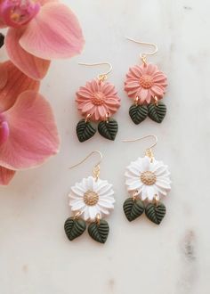 three pairs of dangle earrings with flowers and leaves on them next to a pink flower