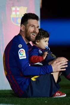 a man sitting on the ground with a child in his lap and wearing a soccer uniform