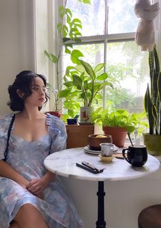 a woman sitting at a table in front of a potted plant next to a window