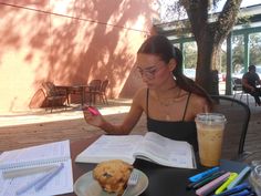 a woman sitting at a table in front of an open book while looking at her cell phone