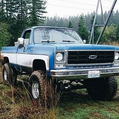 an old blue and white truck parked in the grass next to some power lines with trees in the background