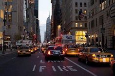 a city street filled with lots of traffic next to tall buildings in the evening time