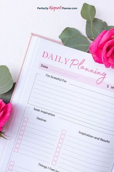 a pink rose sitting on top of a white table next to a daily planning book