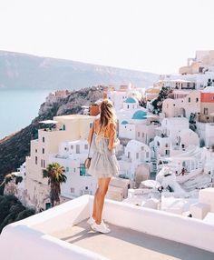 a woman standing on top of a white building next to the ocean with buildings in the background