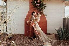 a bride and groom standing in front of a brick wall with flowers hanging from it