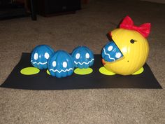 a yellow chicken and three blue eggs sitting on top of a black mat next to each other