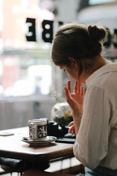 a woman sitting at a table in front of a coffee cup with her hands up