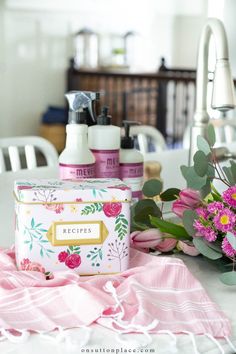 some pink flowers are sitting on a table next to two bottles of lotion and soap