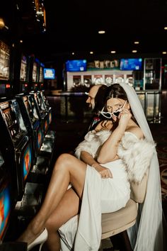 two women in white dresses sitting next to each other on the phone at a slot machine