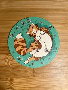 an image of a cat hugging another cat on a wooden surface with flowers around it