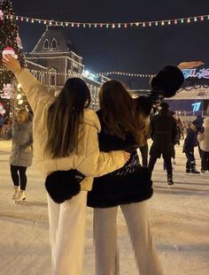 two women are standing in the snow with their arms around each other and one is holding her hand up