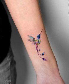 a small hummingbird tattoo on the wrist is shown in blue and purple colors, with an