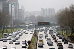 a highway filled with lots of traffic next to tall buildings in the distance and trees on both sides