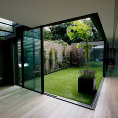 an open room with glass walls and grass in the center, leading to a small garden