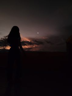 the silhouette of a woman standing in front of a dark sky at night with an orange moon behind her