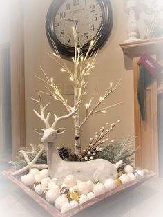 a white deer statue sitting next to a clock on top of a wooden table covered in snow