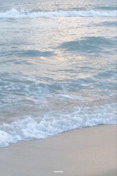 a person walking on the beach with a surfboard in their hand and waves coming toward them