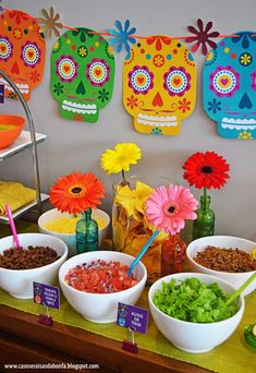 a table topped with bowls filled with food next to colorful paper sugar skull wall hangings