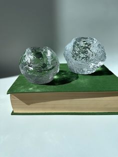 two glass bowls sitting on top of a green cloth covered book with shadows coming from the pages