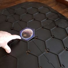 a hand pointing at an object that is on top of a black table with hexagonal tiles