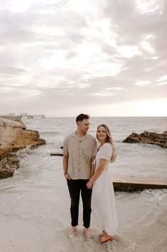 a man and woman standing in the water at the beach with their arms around each other