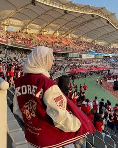 a person in a red and white jacket sitting on a bleachers watching a game