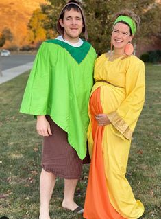 two people dressed up in costumes standing next to each other on the grass with trees in the background