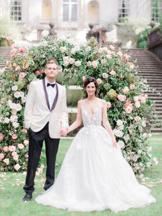 a bride and groom holding hands in front of a floral arch