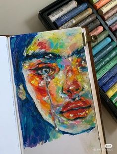 an art journal with colored crayons next to it and a painting of a woman's face