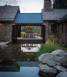 an outdoor dining area next to a pond with lights on the tables and chairs in it