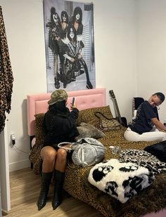 a man and woman sitting on a bed in a room with leopard print sheets, black boots, and a pink headboard