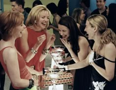 four women laughing around a table with a cake on it and people looking at it