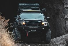 the front end of a black vehicle driving through a tunnel with rocks and grass in the background