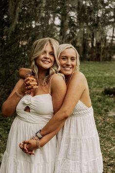 two women in white dresses standing next to each other and smiling at the camera with their arms around one another