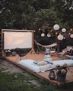 an outdoor movie screen is set up on a wooden deck surrounded by lights and furniture