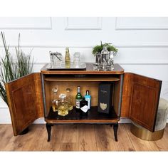 a cabinet with liquor bottles and glasses on it in front of a white wall next to a potted plant