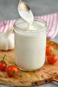 a spoon full of mayonnaise on top of a cutting board with tomatoes and garlic