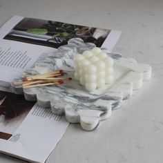 a marble tray with matches and toothpicks sitting on it next to an open book