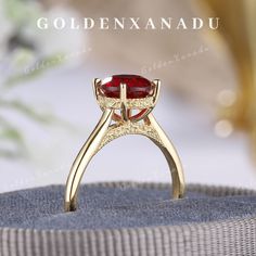 a gold ring with a red stone in the center on top of a cushioned surface