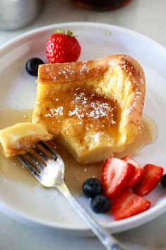 a piece of french toast on a plate with strawberries and blueberries next to it